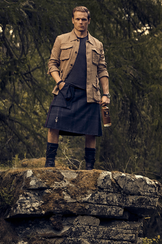 Sam Heughan on a cliff top holding a bottle of The Sassenach Whisky